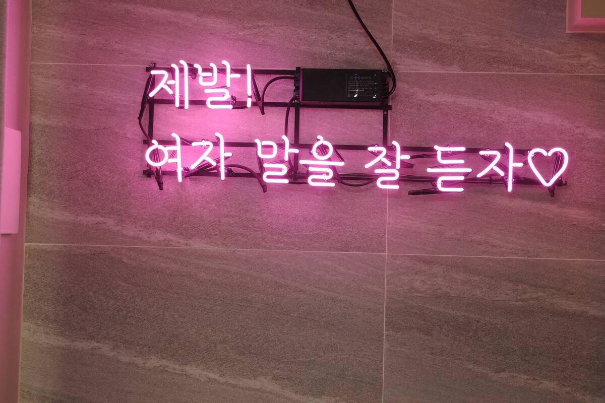 A neon sign with Korean text on a pink wall.