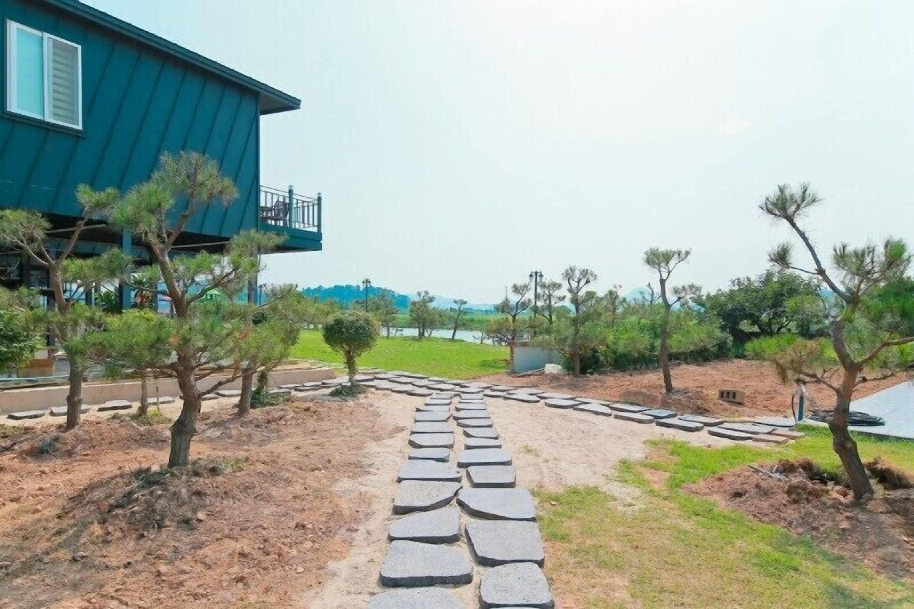 A pathway leading to a blue building with a balcony, surrounded by trees and a grassy area.