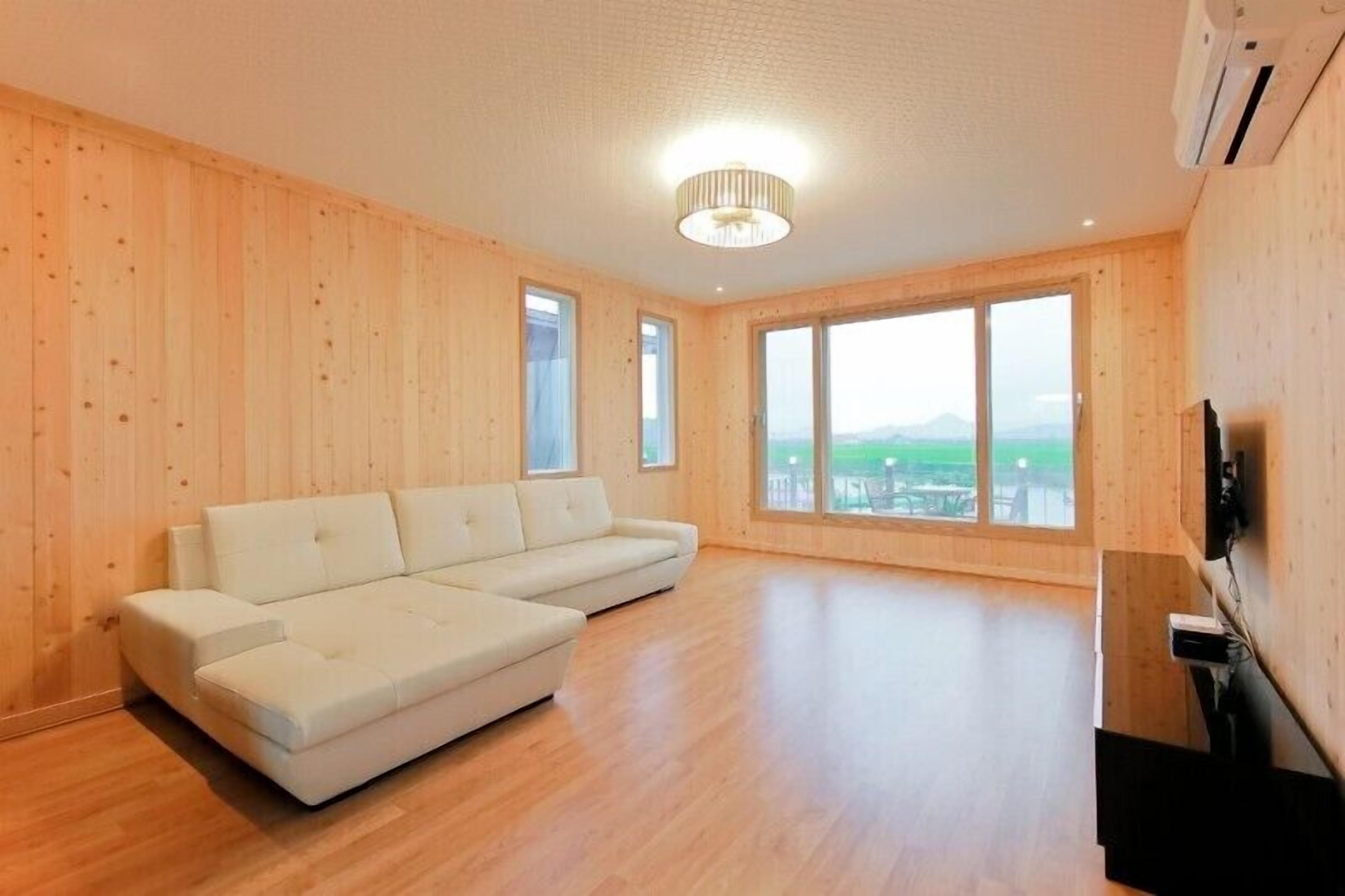 Habitación amplia con un sofá seccional grande, paredes de madera y ventanas grandes que dan a vistas del exterior.