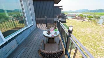 A balcony with wicker furniture, a table with a glass, and a view of a river and fields.