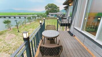 A balcony with wicker furniture and a view of a river and fields.