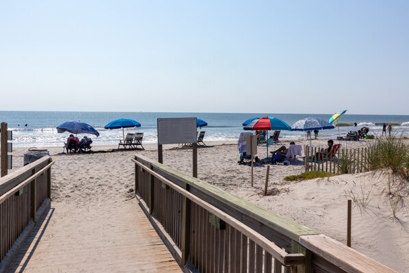 Walk along the beachside boardwalk to the shoreline, where umbrellas provide shade and beach chairs await.