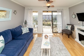 Relax in a spacious living room with a sofa, coffee table, and fireplace, offering a view of the outdoor balcony with a table and chairs.