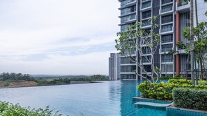 A modern hotel with a large infinity pool, surrounded by lush greenery and offering views of distant buildings. - OYO Home 89725 Beautiful 3br Grand Medini (Iskandar Puteri)