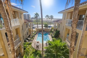 A pool area with a view of the ocean, surrounded by palm trees and a building with balconies.