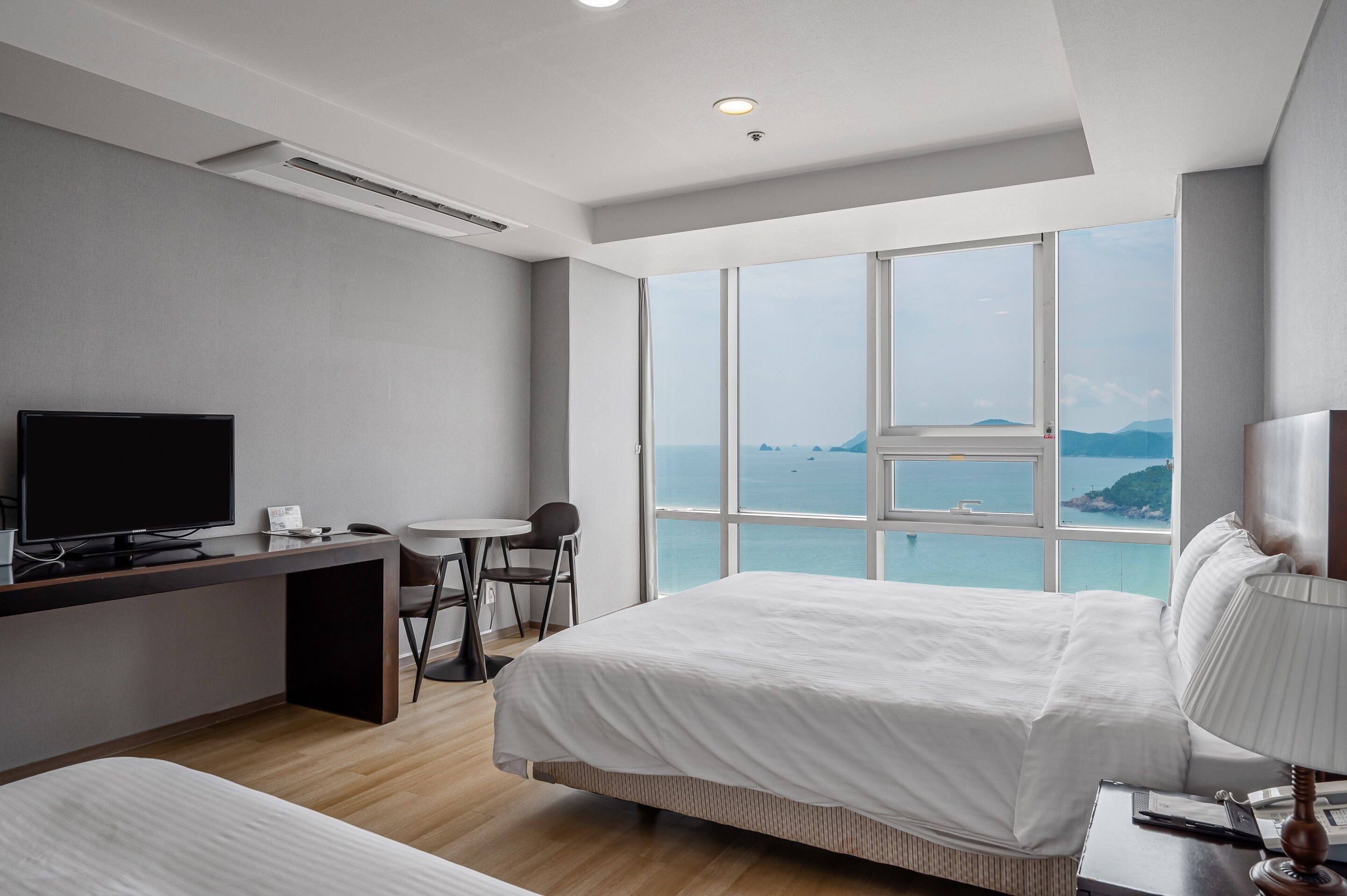 Habitació d'hotel moderna amb un llit gran, una taula de treball amb un ordinador, una cadira i vista al mar.
