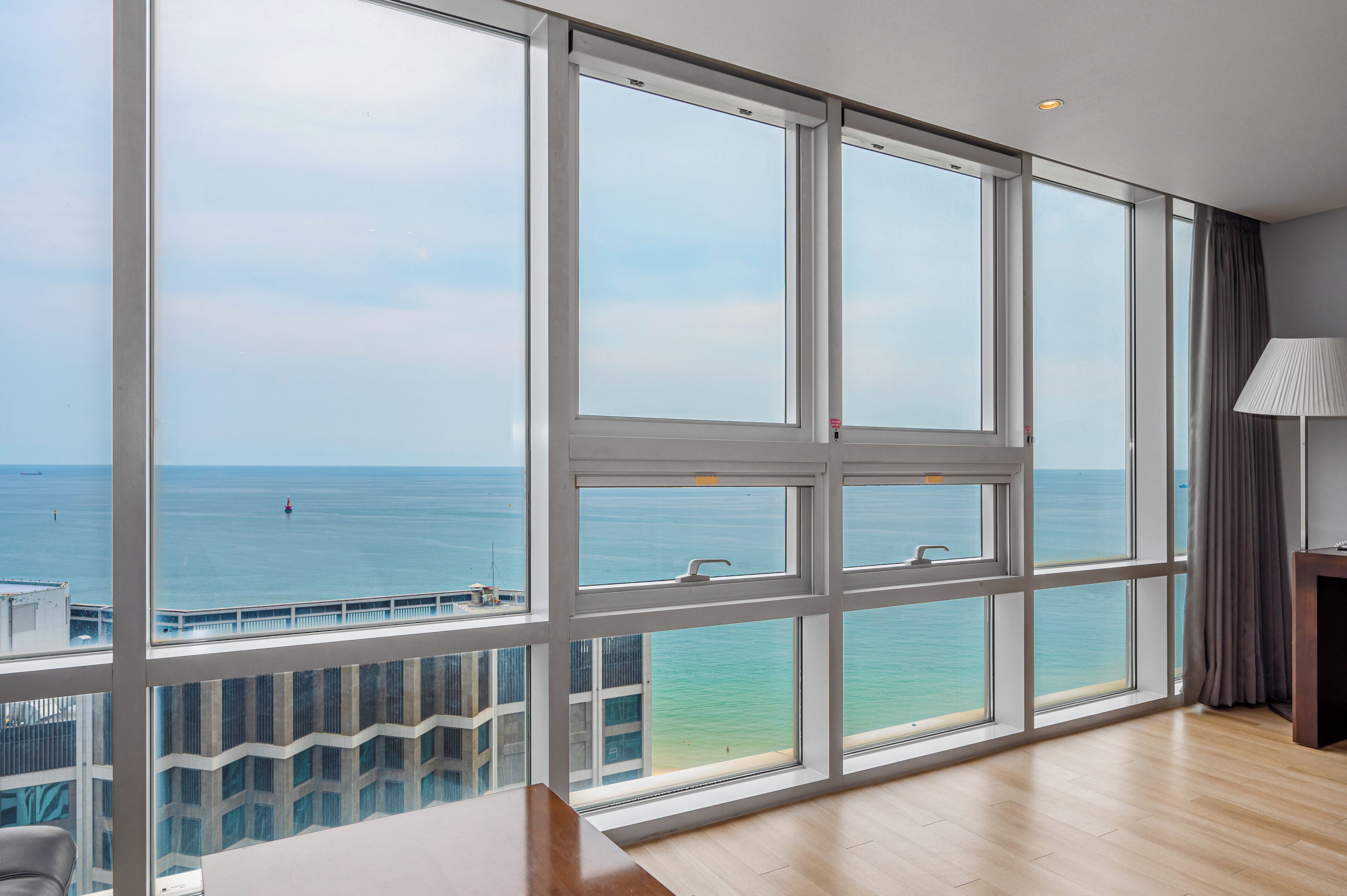 A room with large windows, a view of the sea, a wooden floor, and a lamp.