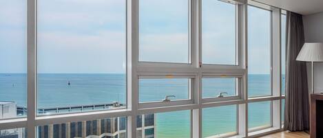 A room with large windows, a view of the sea, a wooden floor, and a lamp.