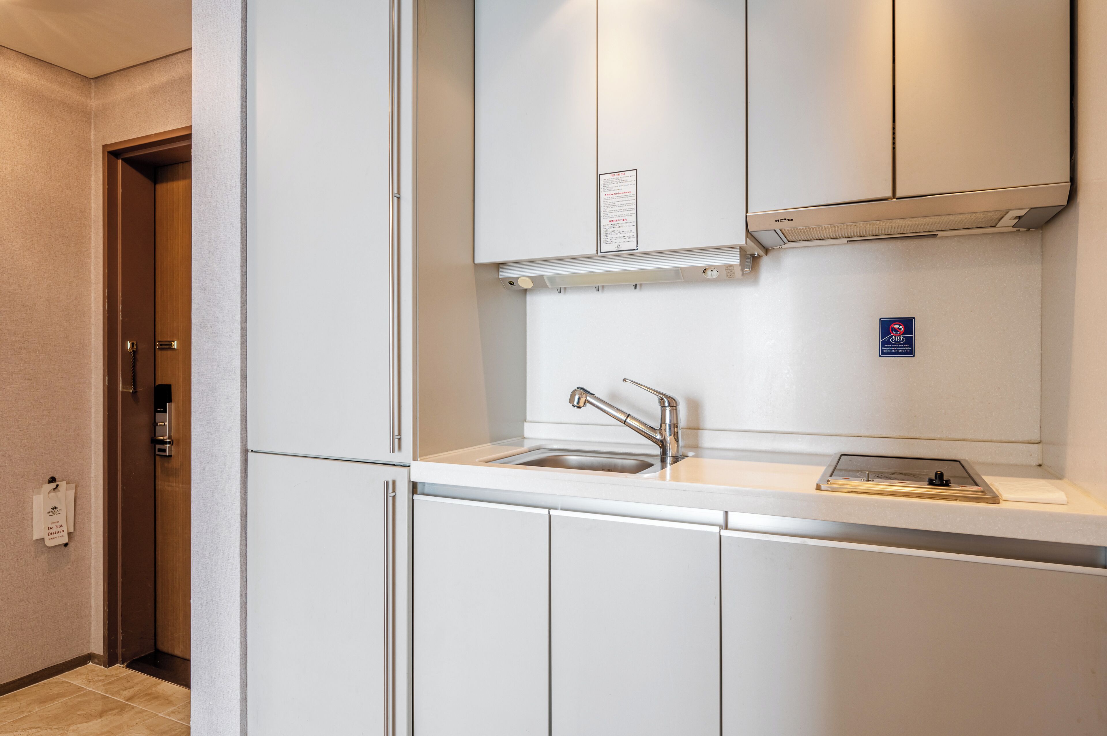 A kitchenette with white cabinets, a stainless steel sink, and a built-in range hood.