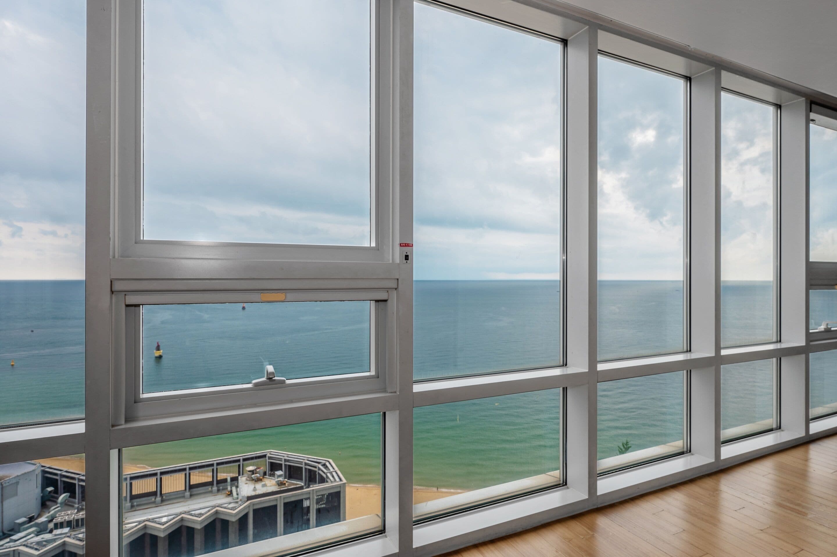 A room with large windows overlooking the sea, a view of the ocean, and a balcony with a railing.