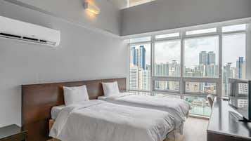 A modern hotel room with two beds, a large window with a city view, and a flat-screen TV.