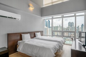 A modern hotel room with two beds, a large window with a city view, and a flat-screen TV.