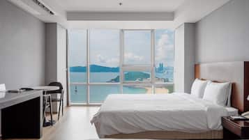 A hotel room with a large bed, a desk, and a view of the sea.