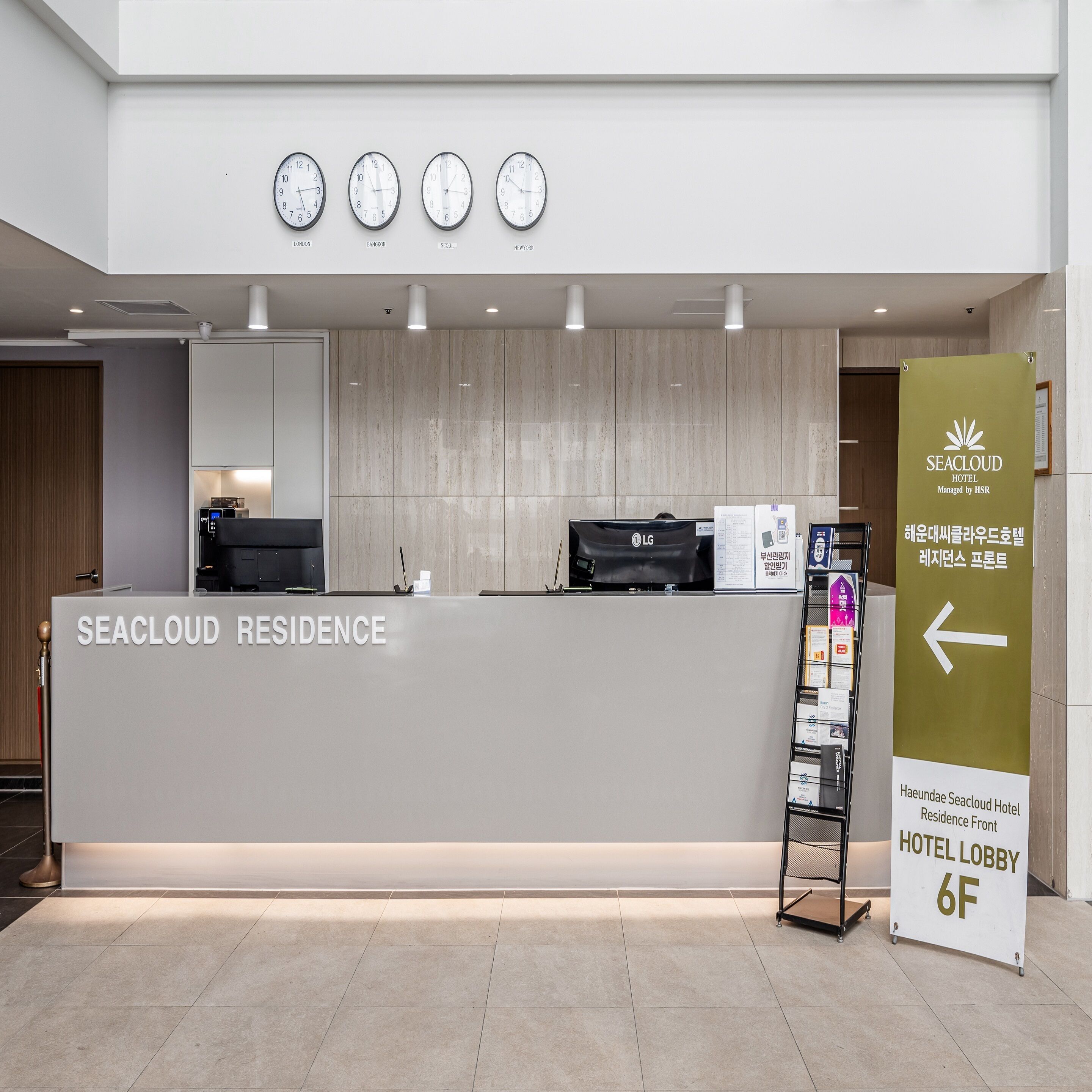 A hotel reception desk with clocks displaying different time zones, a sign indicating the hotel lobby, and a directory stand.