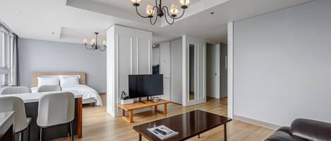 A modern hotel room with a bed, a TV on a wooden stand, a dining area with chairs, a coffee table, and a large mirror.