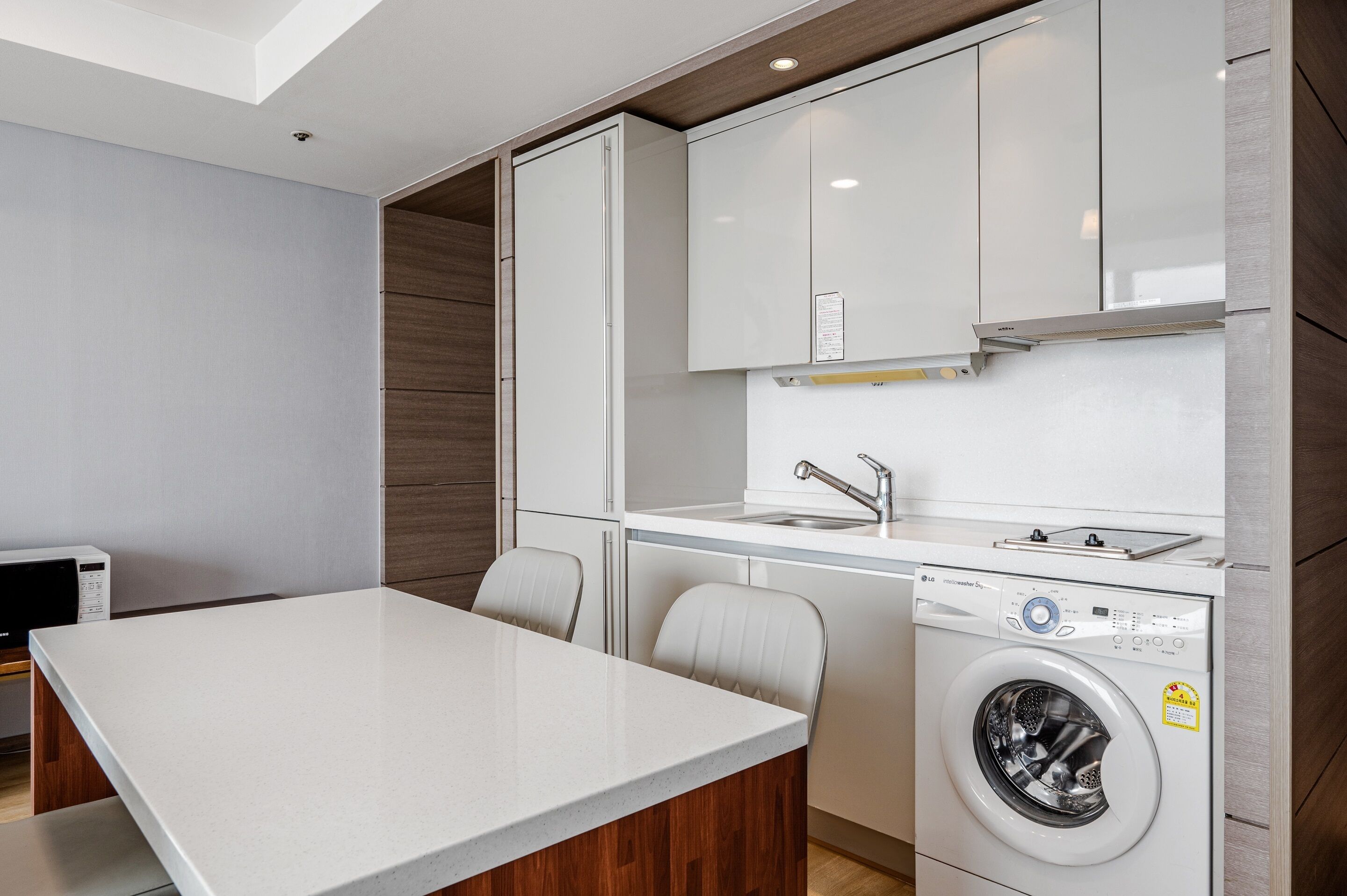 Una cocina moderna con armarios blancos, lavadora integrada y un comedor con mesa y sillas blancas.