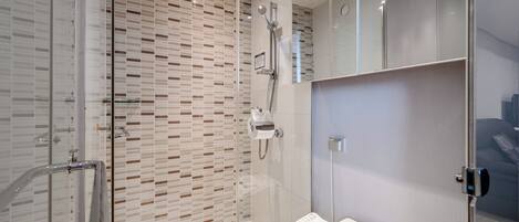 A modern bathroom with a glass shower enclosure, a white toilet, and a mirror above the sink.