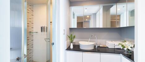 Un baño moderno con cabina de ducha de vidrio, un lavabo blanco sobre encimera negra y un espejo grande sobre el lavabo.