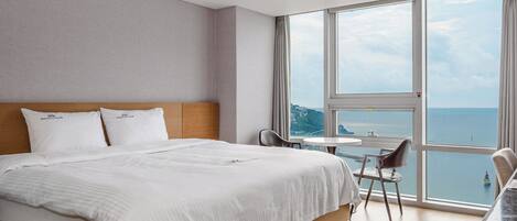 Habitación de hotel con una cama grande, una mesita pequeña, una silla y vista al mar.