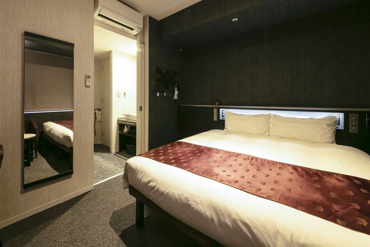 Una habitación de hotel con cama, escritorio, silla, espejo y armario.