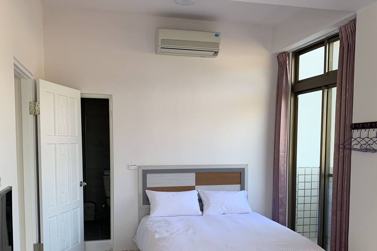Een hotelkamer met een bed, een bureau met stoel, een televisie en een airconditioning.