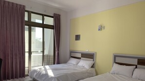 Une chambre d’hôtel avec deux lits, une grande fenêtre avec des rideaux et un mur jaune.
