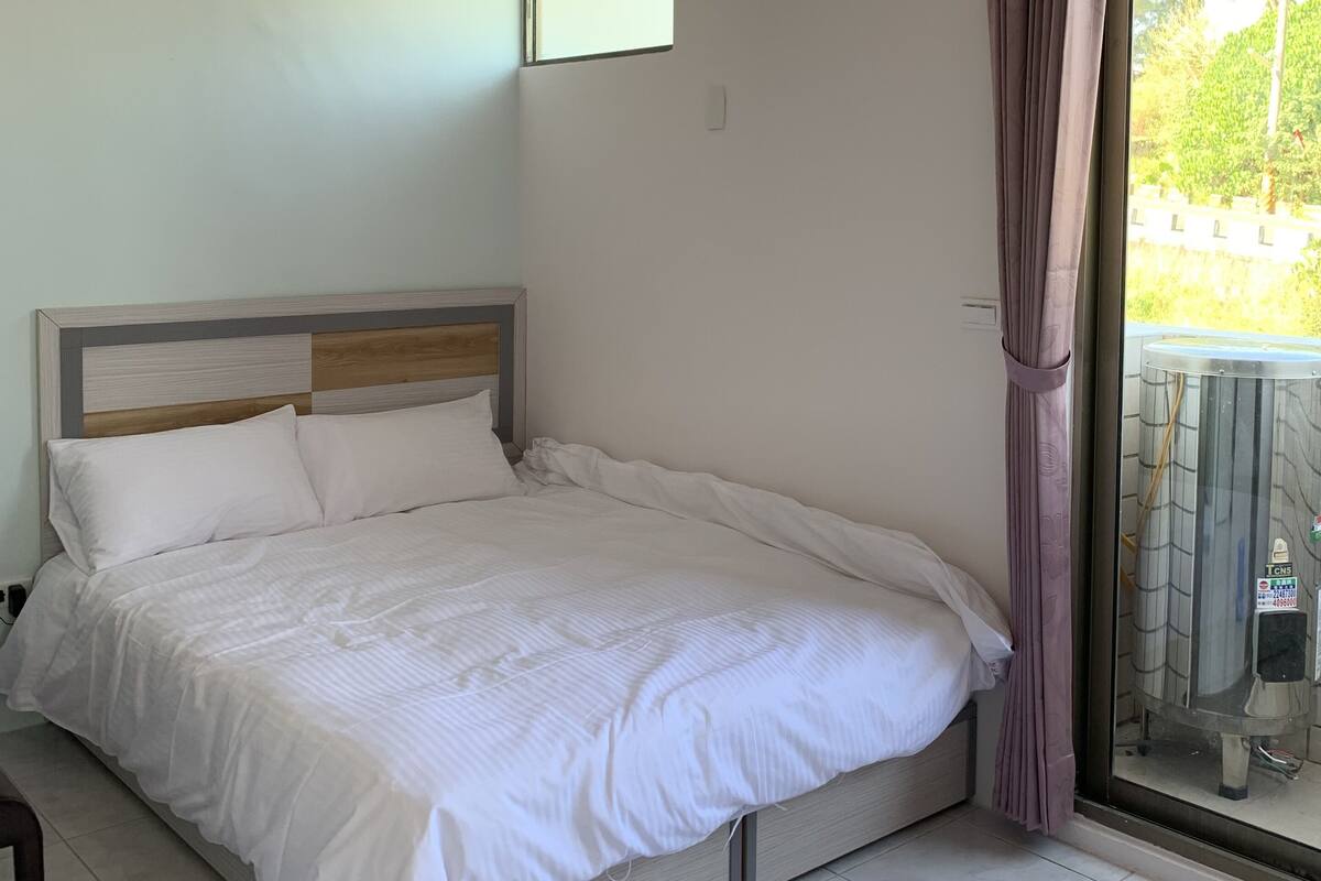 Een slaapkamer met een bed, een raam, een airconditioning en een gordijn.