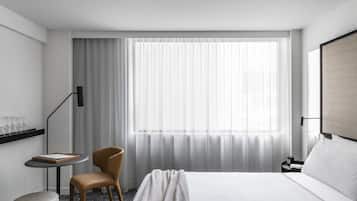 Una habitación de hotel moderna con una cama grande, una pequeña mesa redonda, una silla y una ventana con cortinas translúcidas.