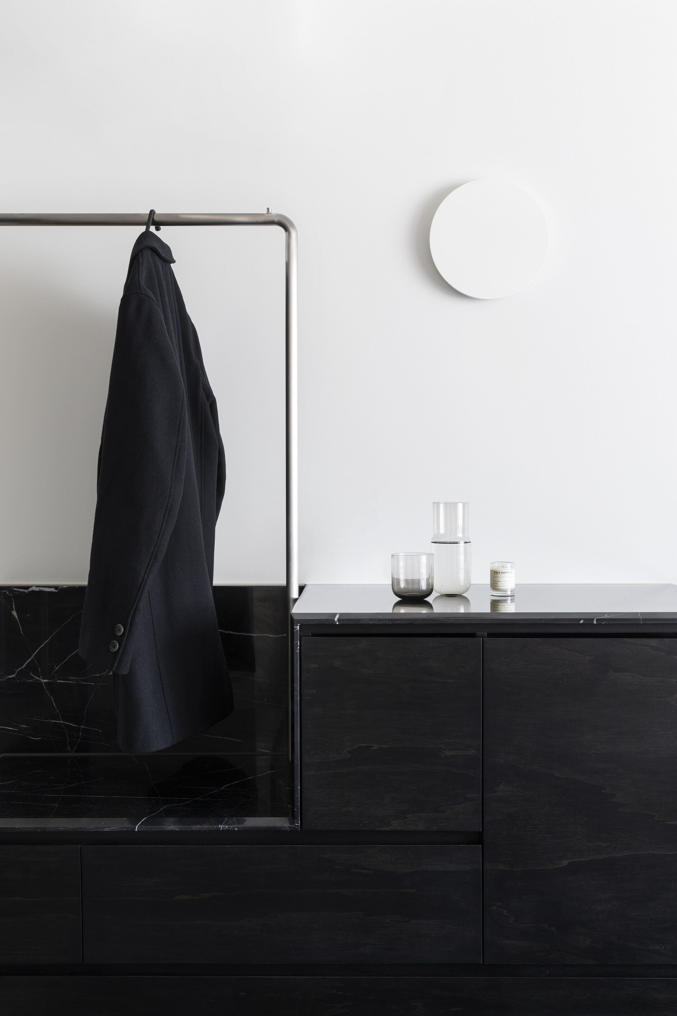 A bathroom with a black marble countertop, a towel rack with a towel, a round mirror, and a small white container.