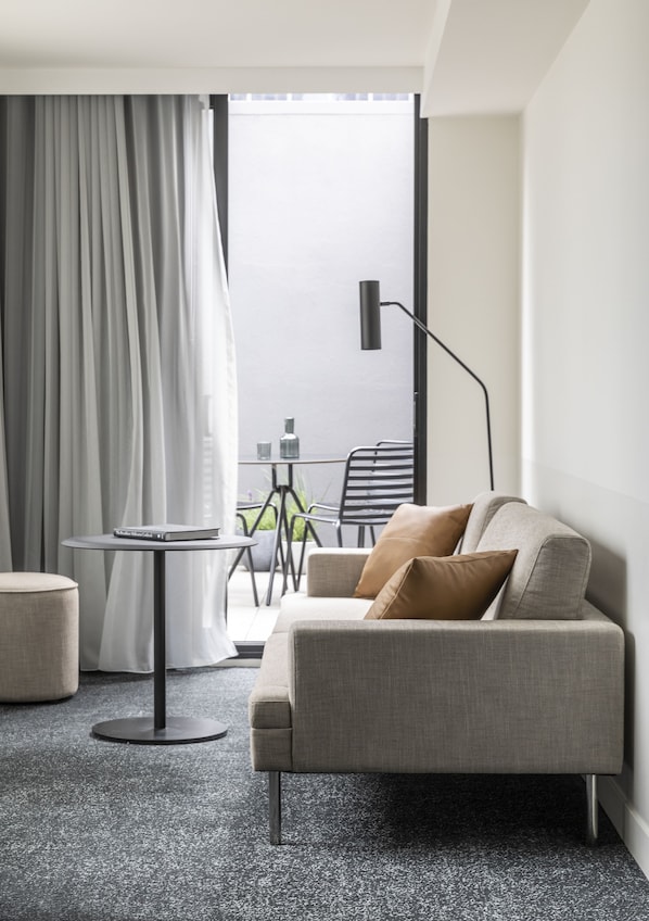 A modern hotel room with a grey sofa, a small round table, a floor lamp, and a view of the outside balcony. - Lancemore Crossley St Melbourne (Melbourne)