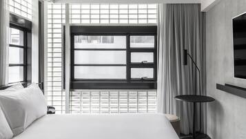 Una habitación de hotel moderna con una cama grande, una ventana con persianas, una mesita redonda y un televisor montado en la pared.
