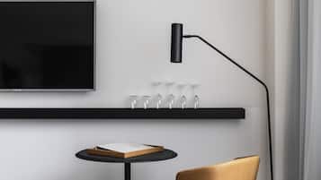 Un intérieur moderne avec un téléviseur fixé au mur, un lampadaire noir, une petite table ronde sur laquelle repose un livre et un fauteuil en cuir.