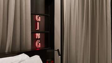 A hotel room with a neatly made bed, a bedside table with a glass, and curtains covering the windows.