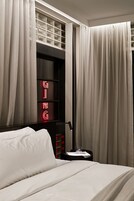 A hotel room with a neatly made bed, a bedside table with a glass, and curtains covering the windows.