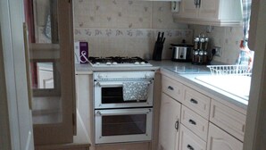 A compact kitchen with a gas stove, oven, and a trash bin. - The Boat House Chalet - Boat of Garten - Near Aviemore - Sleeps 6 (Boat of Garten)