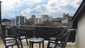 Un balcón con cuatro sillas negras y una mesa redonda pequeña, con vistas a un paisaje urbano con diversos edificios.
