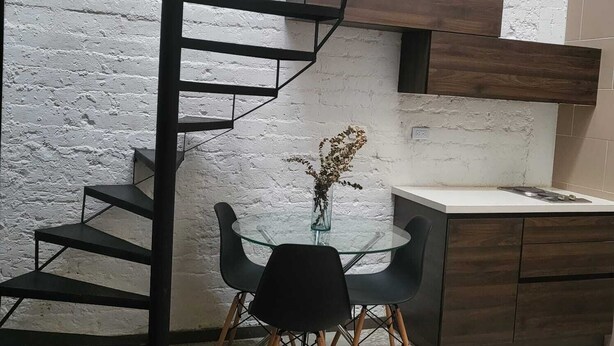 Una cocina moderna con una escalera espiral, una mesa de comedor de vidrio con sillas y una pared blanca con textura.