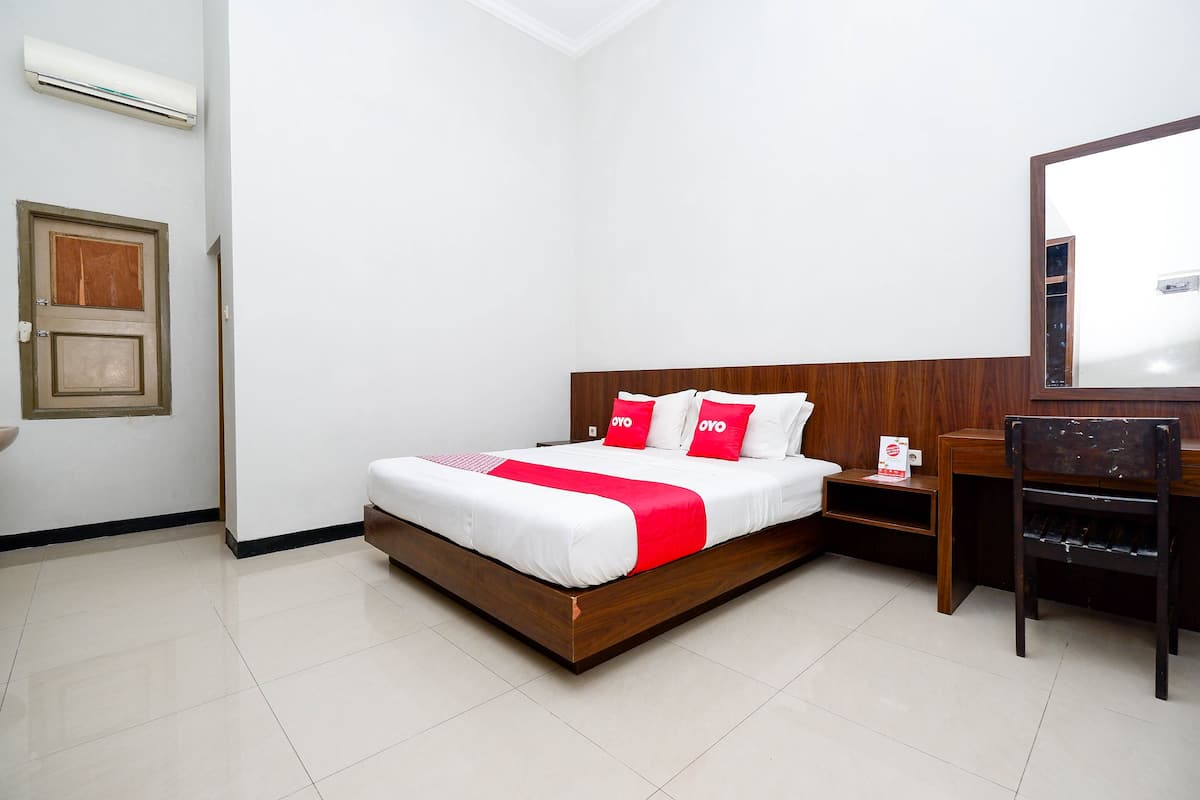 Een hotelkamer met een houten bed, witte muren, een nachtkastje van hout, een bureau en een stoel.