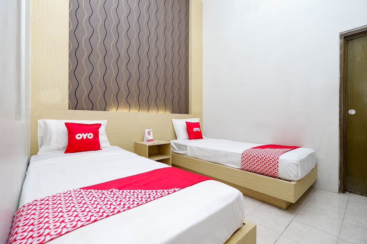 Een hotelkamer met twee bedden, elk voorzien van een wit en rood sprei en een rood kussen met de tekst 'OYO'.