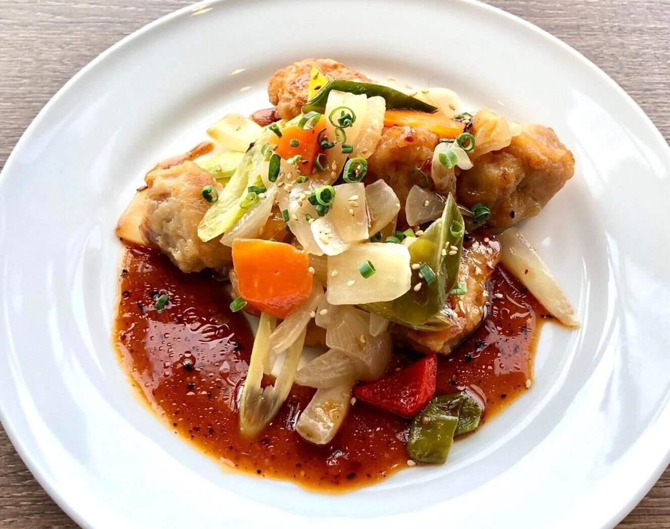 A white plate with a dish of chicken, vegetables, and a red sauce.