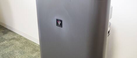 A gray, ribbed, portable air purifier with a control panel and a logo on the front.