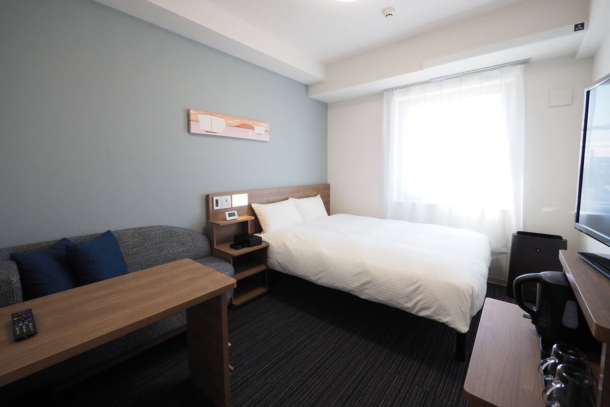A hotel room with a bed, a sofa, a desk, and a coffee machine.