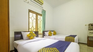 A hotel room with two beds, each with white bedding and decorative pillows. There is a window with a metal grille and a curtain, and a small wooden cabinet with a water dispenser. - SPOT ON 2395 Hotel Aden 2 Syariah (Tasikmalaya)