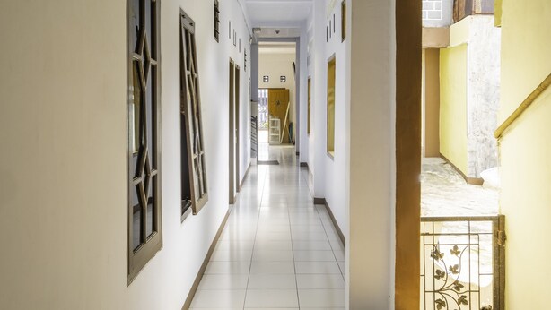 A corridor with white walls and a tiled floor, leading to a staircase and an open area. - SPOT ON 2395 Hotel Aden 2 Syariah (Tasikmalaya)