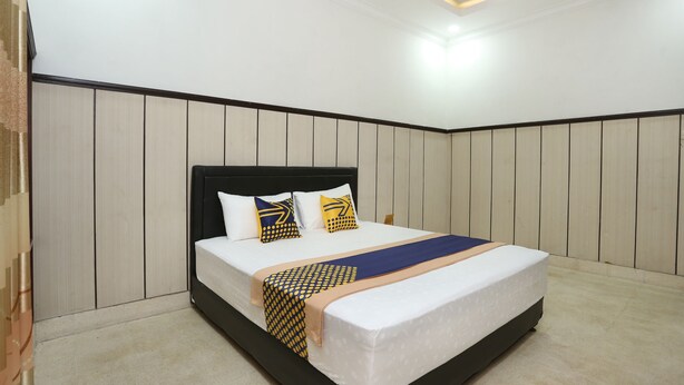 A neatly arranged bedroom with a bed, white walls, and a wooden panel design. - OYO 2268 Tim-tim Homestay SyariahNearUniversitas Gadjah Mada (Depok)