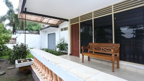 A wooden bench on a balcony with a white railing, a door, and a window with blinds. - OYO 2268 Tim-tim Homestay SyariahNearUniversitas Gadjah Mada (Depok)