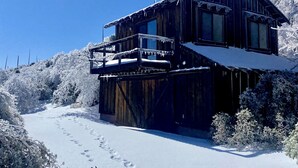 Eine Holzhütte mit einem Balkon, umgeben von schneebedeckten Bäumen.