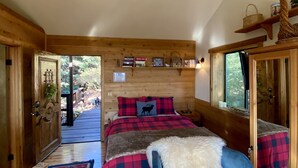 Ein Schlafzimmer in einer Holzhütte mit einem Bett, einem Teppich und einer Holztür, die nach draußen führt.