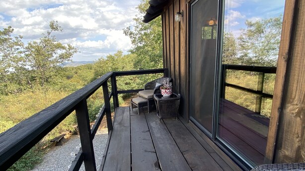 Eine Holzterrasse mit Geländer, eine Sitzecke mit Kissen und Blick auf die umliegende Landschaft.