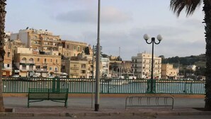 Eine Uferpromenade mit einer grünen Bank, einem Laternenpfahl und einer Reihe von Gebäuden im Hintergrund.